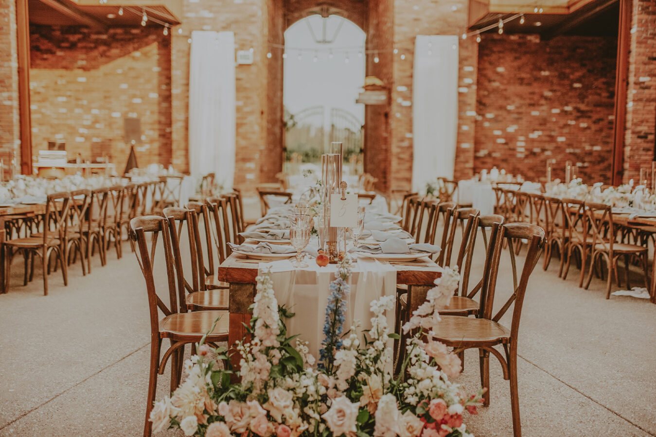 Long tables dressed for a wedding reception, brick walls and string lights above