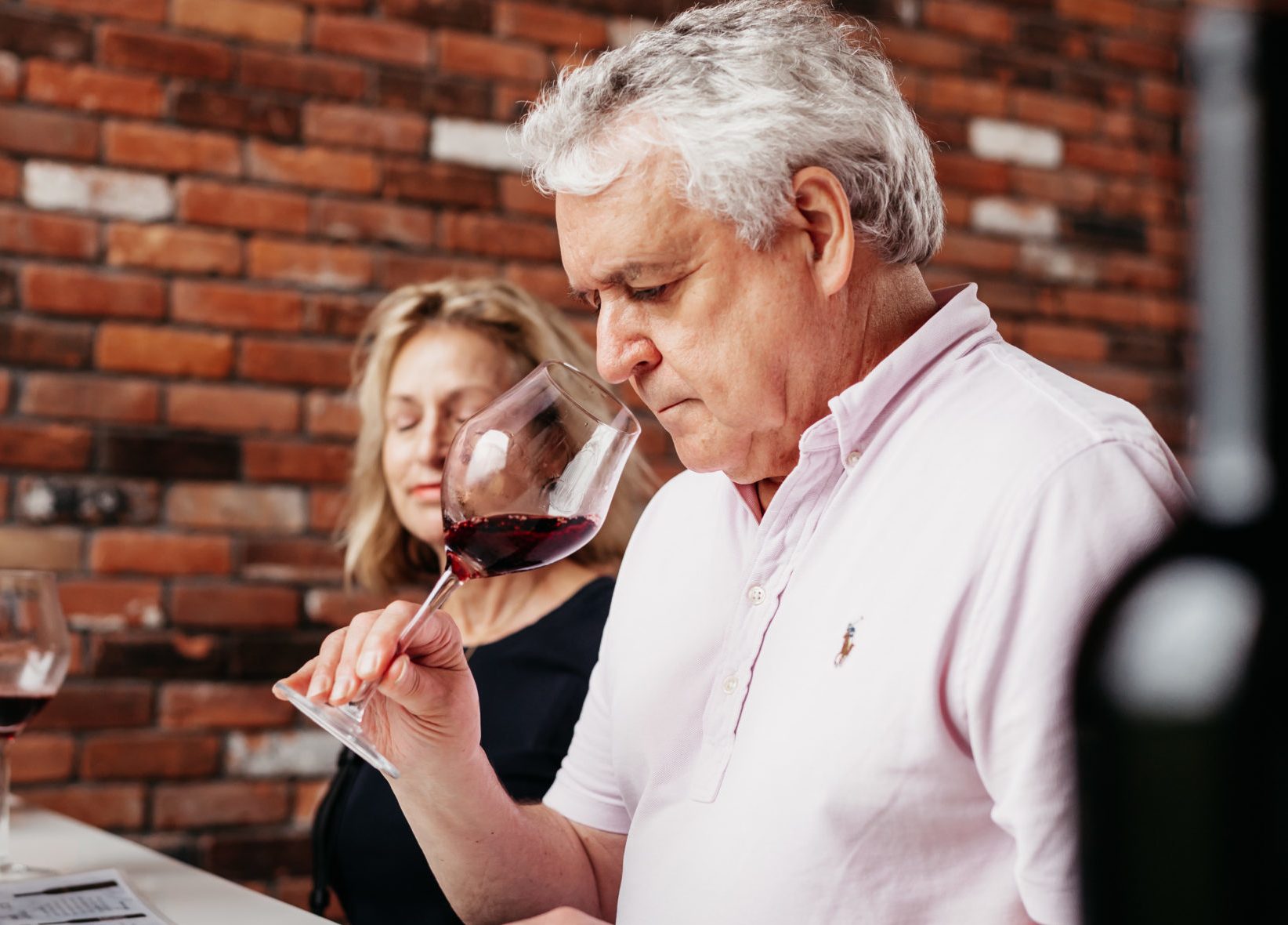 A guest nosing a glass of red against the winery’s brick wall