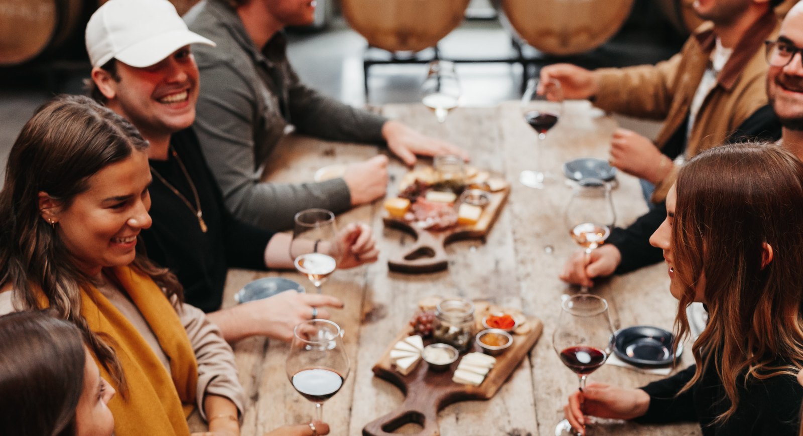 Friends around the long harvest table in the barrel cellar with wine and charcuterie boards