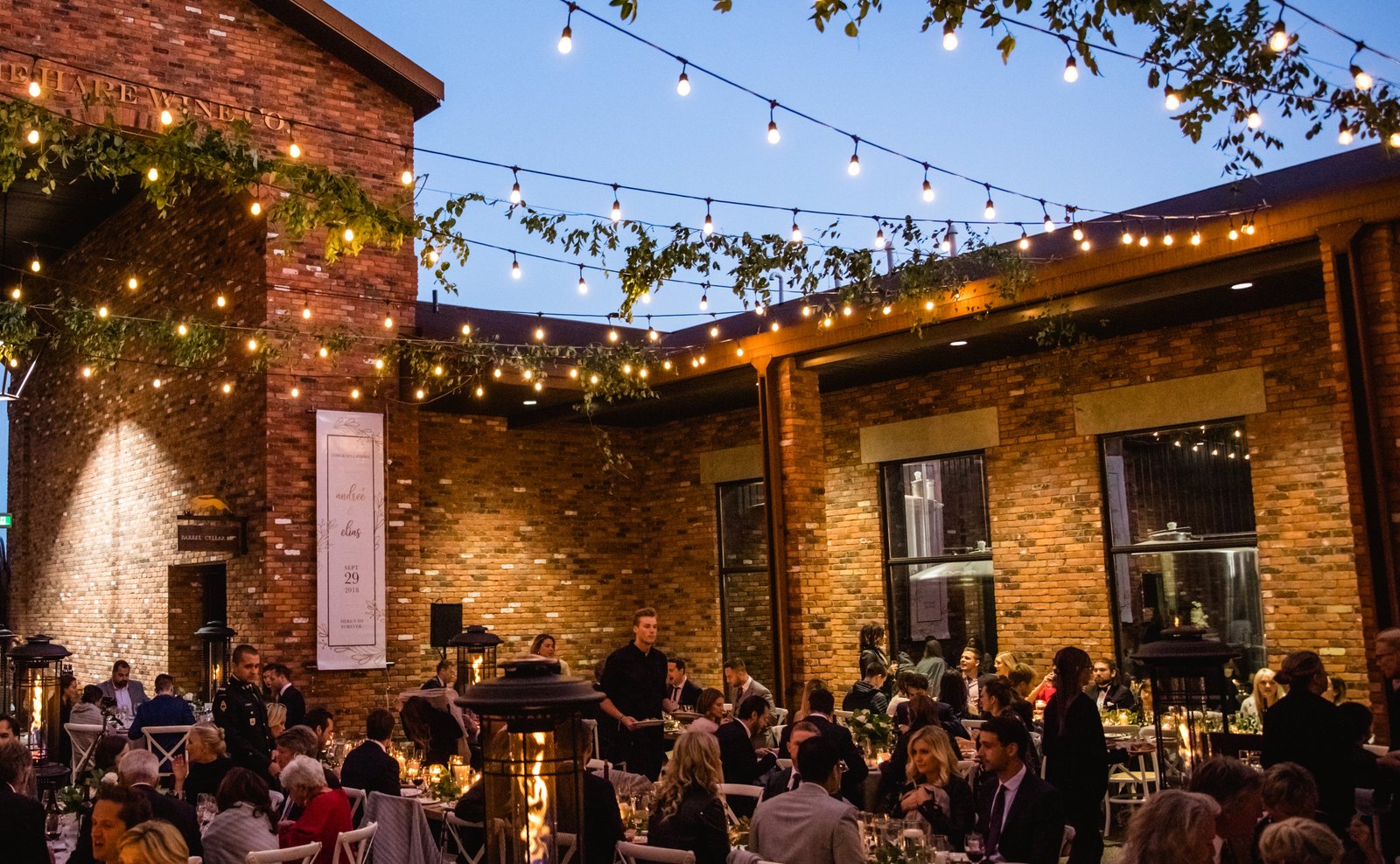 The brick courtyard at dusk, string lights on, set for a reception