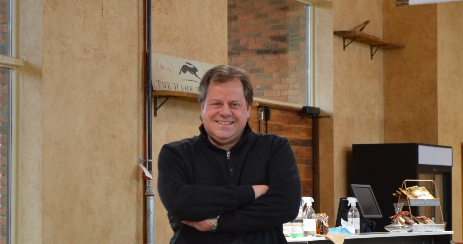 John Hare in the boutique, arms folded, the brick wall behind him